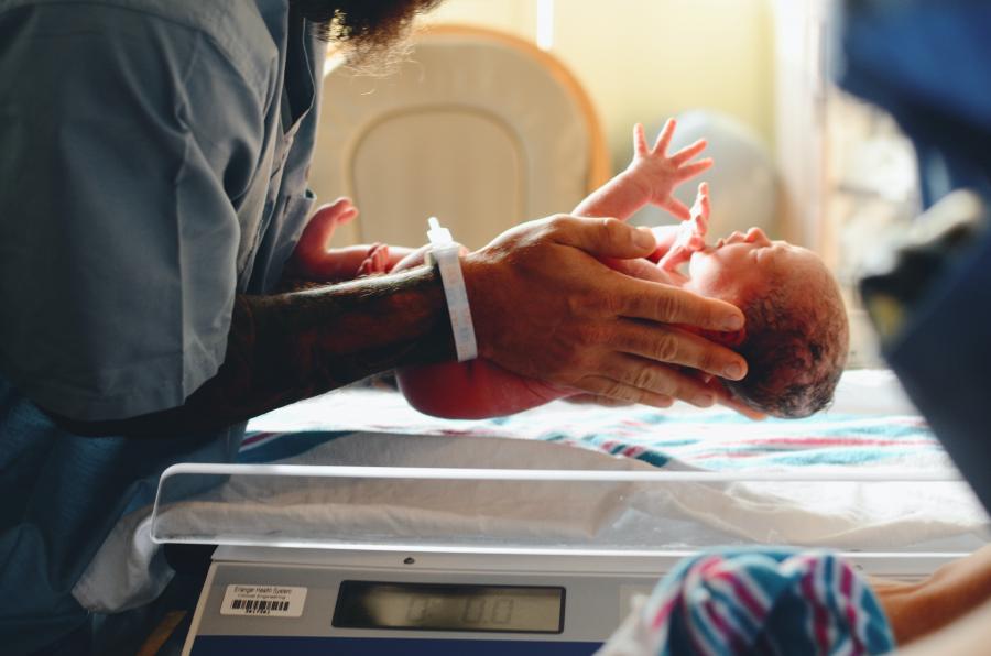 En mand med skæg lægger forsigtigt et nyfødt barn på hospitalsvægten. 