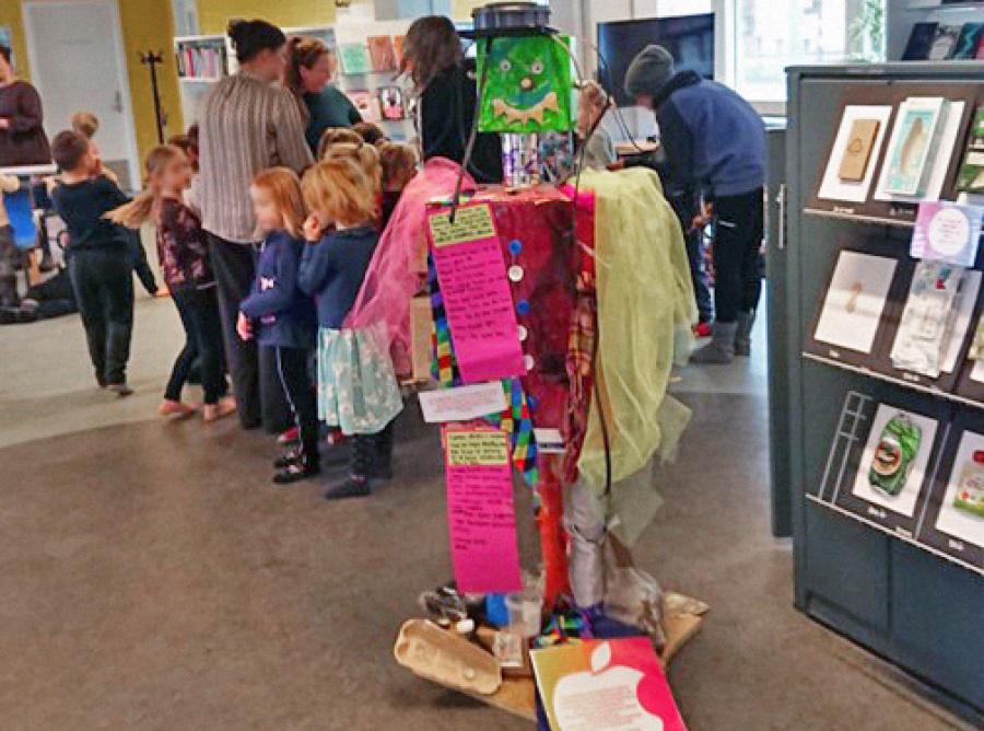 En robot lavet af affald udstillet på Nørresundby Bibliotek. I baggrunden ses børn og deres pædagoger.