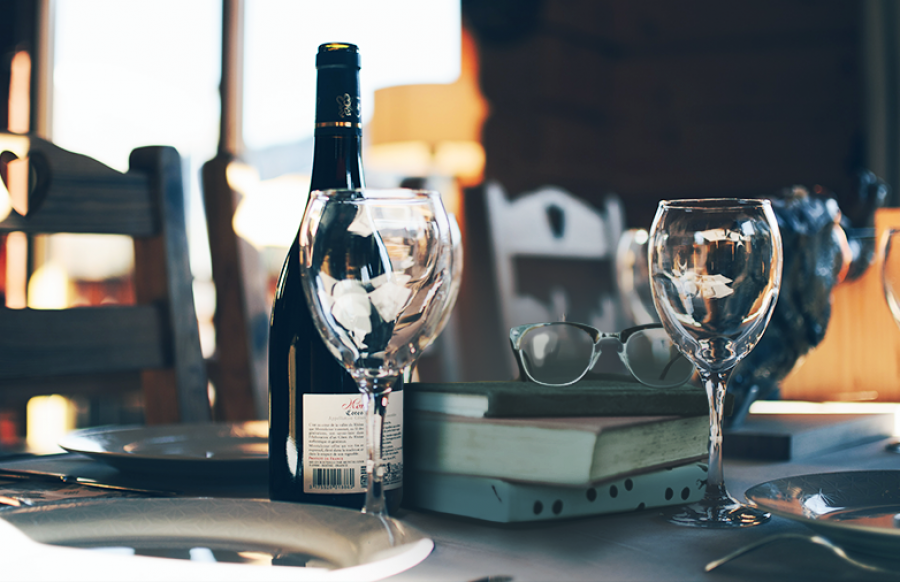 Vinflaske, glas, bøger og briller på et dækket bord