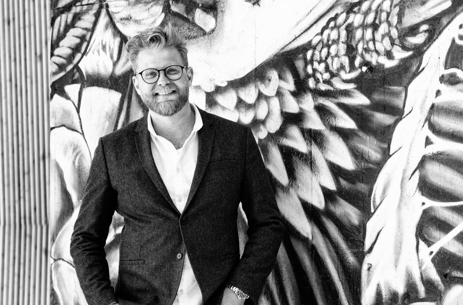 manden bag Bæredygtig Business, Steffen Max Høgh, står og smiler foran en væg med et gadekunstværk på