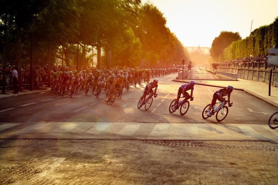 En felt af cyklister kører rundt i et sving på Champs-Élysées i Paris.