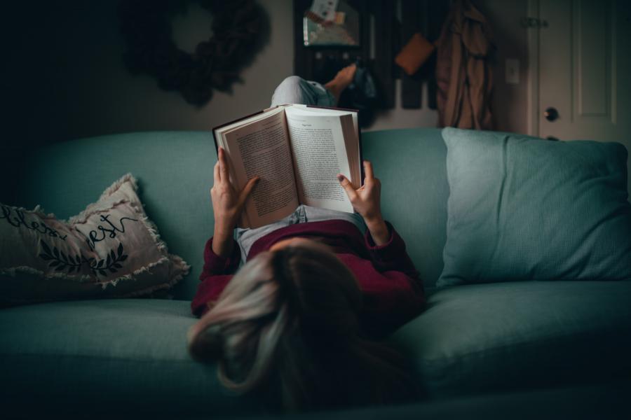 Kvinde ligger omvendt i sofa og læser en bog