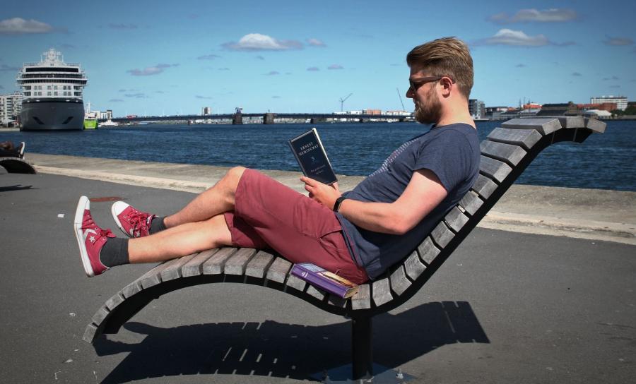 Mand sidder ved havnefronten og læser 