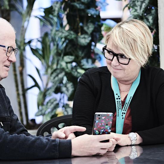 To personer sidder og kigger på en mobiltelefon