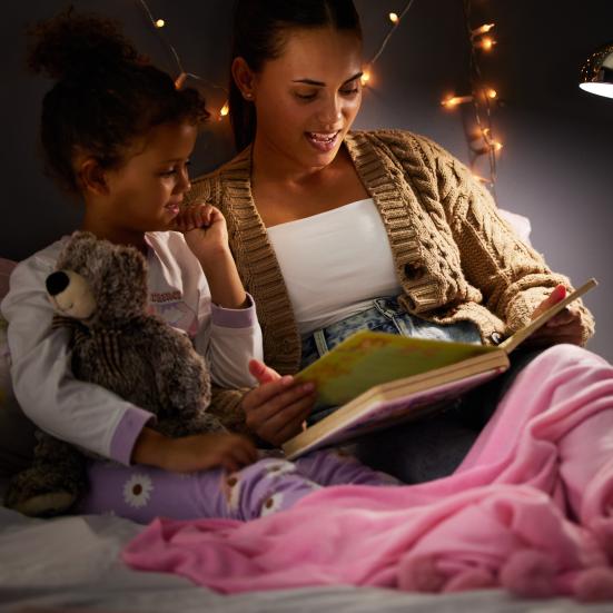 Mor og barn sidder i seng og læser 