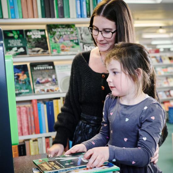 En voksen og et barn står i et bibliotek foran en udlånsautomat