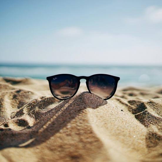 Billede af solbriller på sandstrand. Foto: Ethan Robertson, Unsplash.