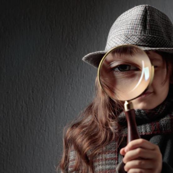 Pige med hat holder lup op foran øjet.