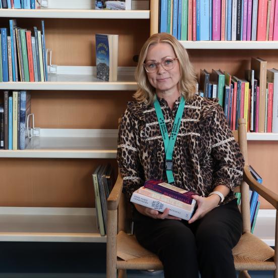 Pia sidder i en lænestol foran en bogreol med de tre omtalte bøger i hænderne.