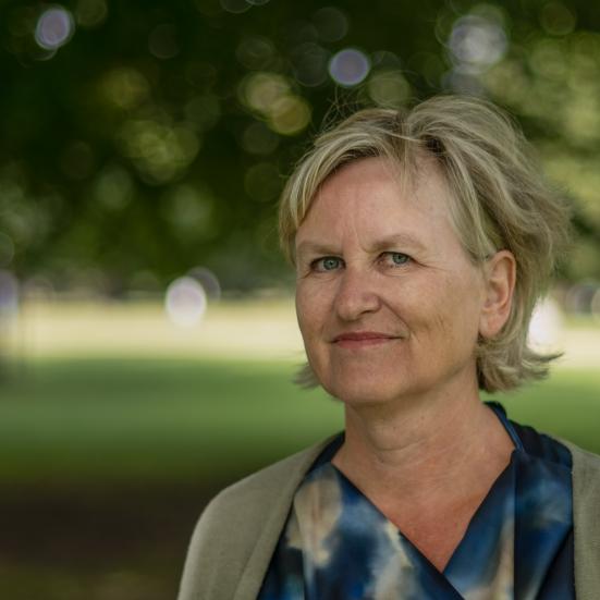 Forfatter Ida Jessen står udendørs i grønne omgivelser. Hun smiler.