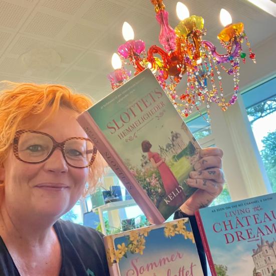 Maria viser tre af de omtalte bøger i artiklen. I baggrunden ses en farvestrålende lampe.