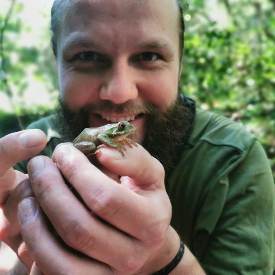 Foto af naturvejleder Mikkel Rødvig, som holder en frø i hænderne frem for sig. Mikkel smiler og kigger ind i kameraet.