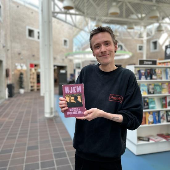 Søren Malthe står med den omtalte bog i denne artikel i hænderne. Han smiler til kameraet. Baggrunden er let sløret og viser biblioteksrummet.