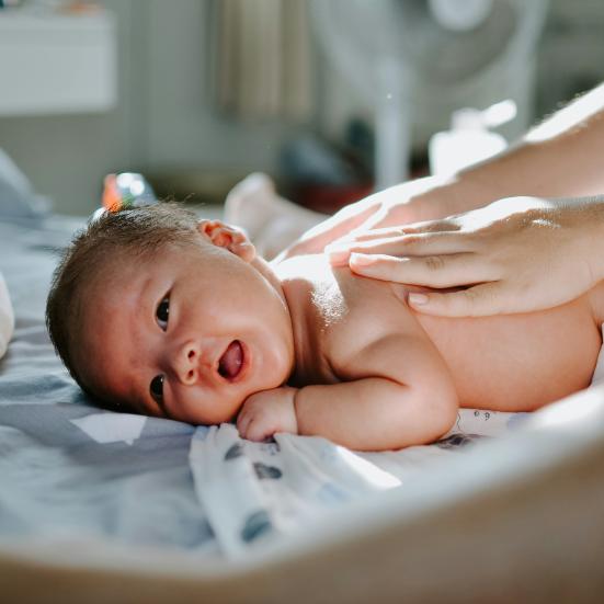 Baby der ligger på maven, mens hænder masserer babyen på ryggen.