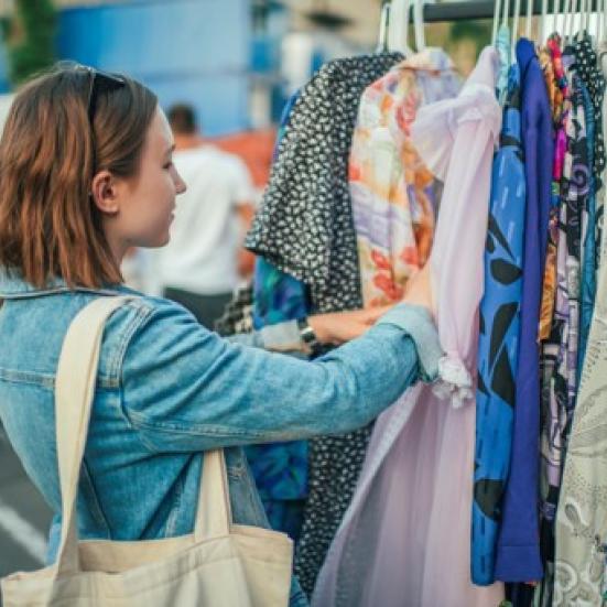 En person står ved en bøjlestang og kigger på forskelligt tøj.