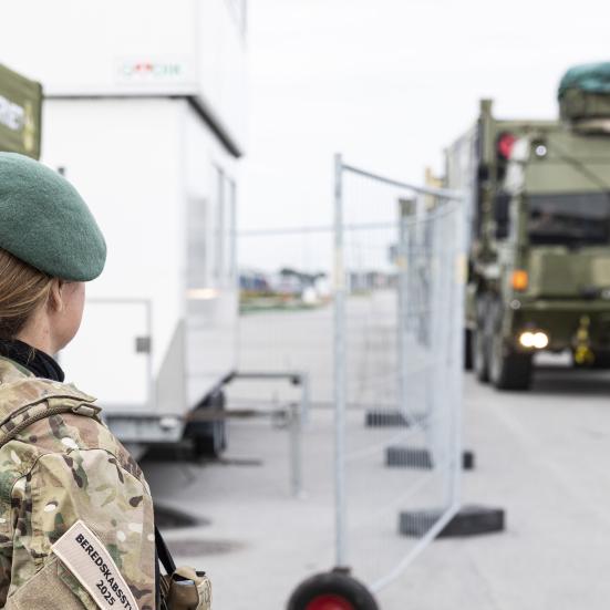 En hjemmeværnssoldat står med ryggen til og kigger på et stort militærkøretøj. 