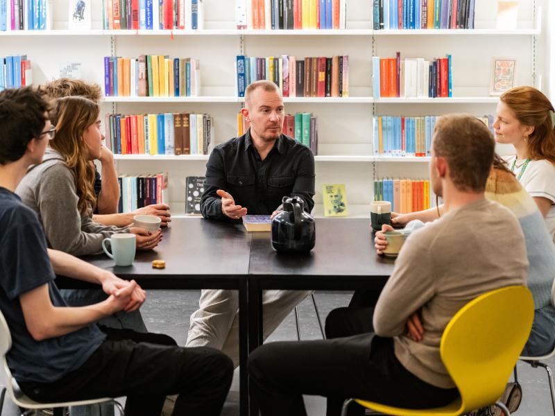 En gruppe mennesker sidder omkring et bord i biblioteket. 