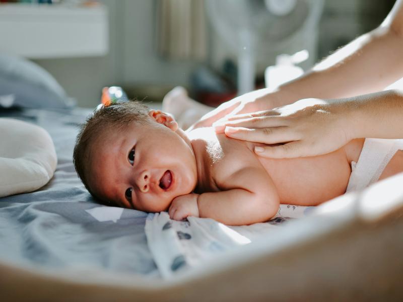 Baby der ligger på maven, mens hænder masserer babyen på ryggen.
