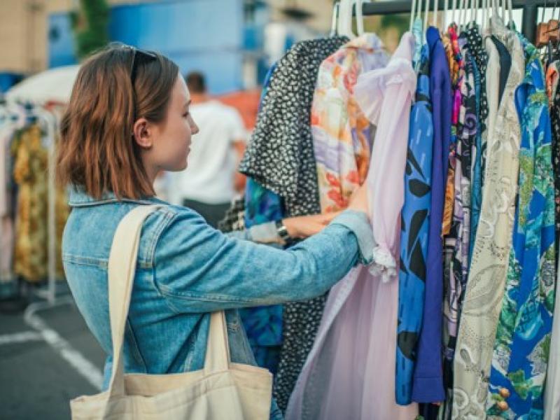 En person står ved en bøjlestang og kigger på forskelligt tøj.