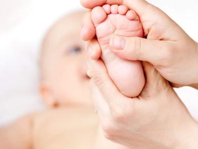 En baby ligger på ryggen med en fod i vejret. En voksen persons hænder masserer foden.
