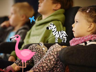 En række børn sidder i biografsæder og kigger mod en skærm. Oven på er tegninger af hhv. en Flamingo og en Zebra