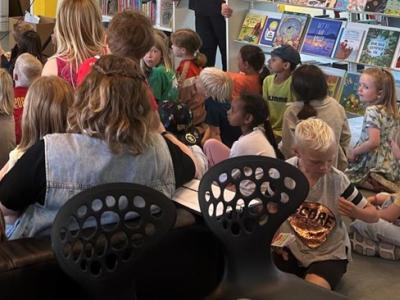 Børn sidder i flok på biblioteket og lytter til højtlæsning
