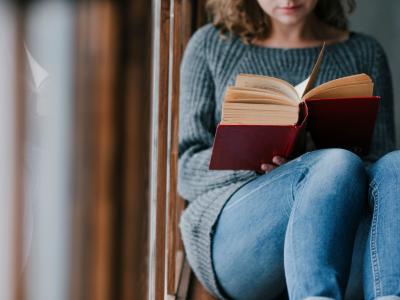 Kvinde der sidder i en vindueskarm og læser