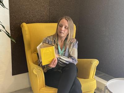 Nina sidder i en gul stol og læser i en bog.