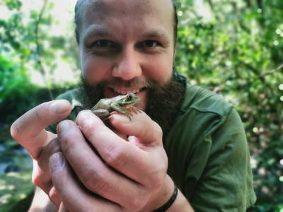 Foto af naturvejleder Mikkel Rødvig, som holder en frø i hænderne frem for sig. Mikkel smiler og kigger ind i kameraet.