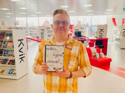 Martin står på Hjørring Bibliotek. Han holder den omtalte bog i denne artikel mellem hænderne. Bag Martin ses biblioteksrummet med fyldte bogreoler og udstillinger.