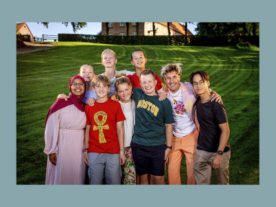 Deltagerne og værten til den store juniorbagedyst på DR står på en grøn græsplæne.