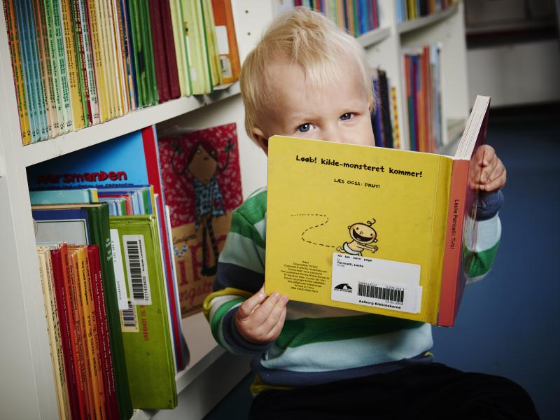 Barn sidder på gulvet foran bøger. Barnet holder en bog i hånden. 