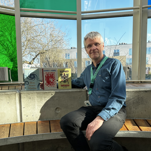 Erling sidder i glashjørnet på Hovedbiblioteket. Ved hans side står alle tre romer, som er omtalt i denne artikel. De står alle med forsiderne fremad, så man kan se dem. Erling smiler og lyser falder smukt ind ad glashjørnets farverige ruder.