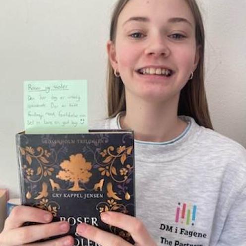 Elev fra 7. klasse der holder bogen "Roser og violer" i hænderne og kigger smilende ind i kameraet