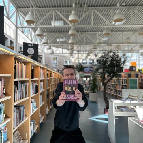 Søren Malthe står blandt fyldte bogreoler og biblioteksudstillinger og holder den omtalte bog i denne artikel frem for sig i strakte arme, så den næste skjuler hans ansigt. Baggrunden er let sløret og viser biblioteksrummet med bl.a. glashjørnet.