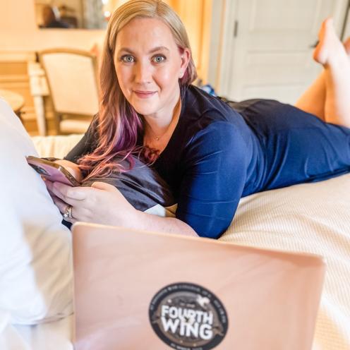 Rebecca Yarros poserer på en seng med sin computer foran sig.