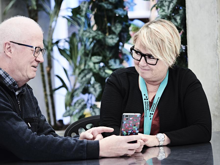 To personer sidder og kigger på en mobiltelefon