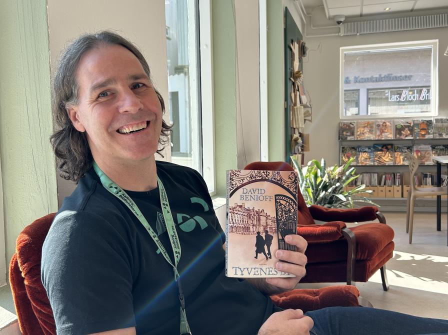 Kenneth sidder i en rød lænestol og viser bogen "Tyvenes by" frem.