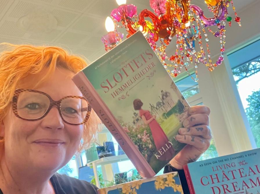 Maria viser tre af de omtalte bøger i artiklen. I baggrunden ses en farvestrålende lampe.