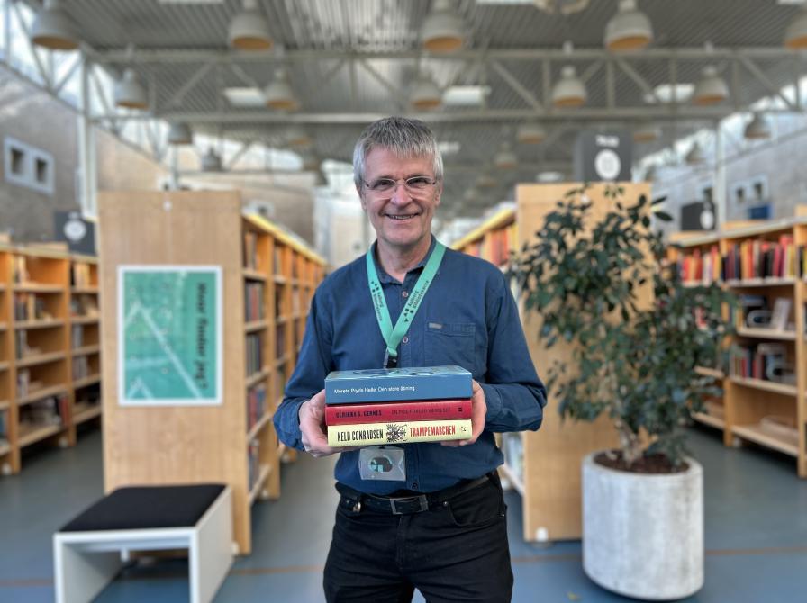 Erling står på Hovedbiblioteket med alle tre bøger, som er omtalt i denne artikel, i hænderne. Erling smiler og baggrunden, der viser biblioteksrummet med fyldte bogreoler, er let slørret.