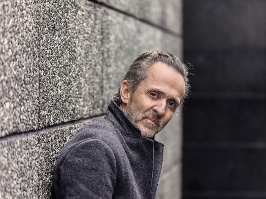 Forfatter Kim Fupz Aakeson står i en frakke og læner sig op ad en grå væg