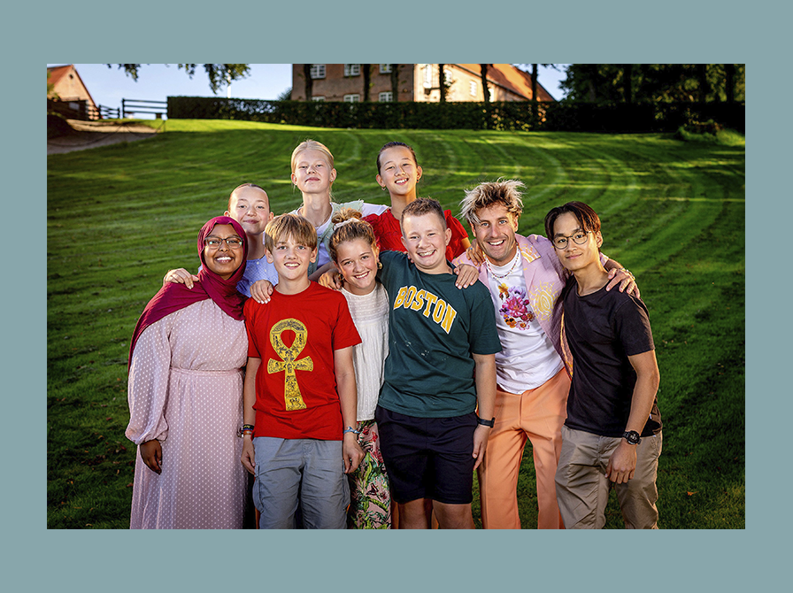 Deltagerne og værten til den store juniorbagedyst på DR står på en grøn græsplæne.