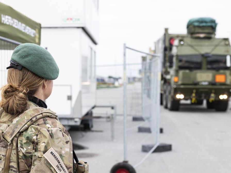 En hjemmeværnssoldat står med ryggen til og kigger på et stort militærkøretøj. 